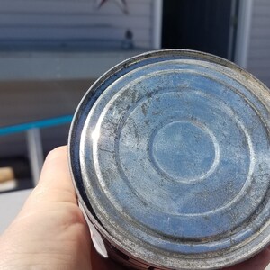 May include: The bottom of a silver metal can with a circular design.