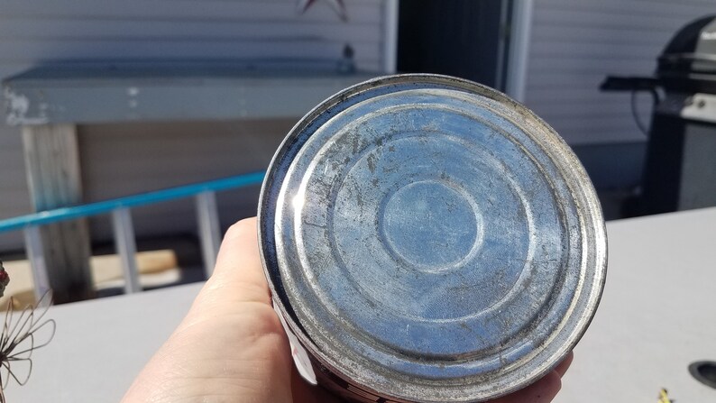 May include: The bottom of a silver metal can with a circular design.