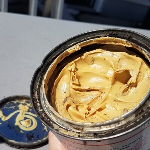 May include: A partially full tin of yellow grease. The tin is dirty and has some rust on it.