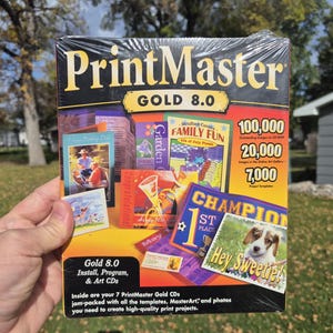 May include: A shrink-wrapped PrintMaster Gold 8.0 software box featuring a black and yellow design. The cover displays various graphic project examples, including a puppy photo with the text Hey Sweetie!, and lists 100,000 images.