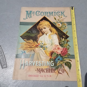 May include: Vintage advertisement for McCormick Harvesting Machine Co. featuring a young girl holding a bouquet of flowers and wheat stalks. The advertisement is printed on a light blue background with a dark blue border and the text "McCormick Harvesting Machine Co. Chicago, Ill. U.S.A." in black.