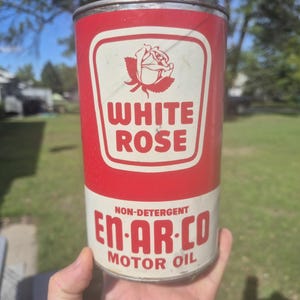 May include: A cylindrical metal motor oil can featuring a red and white color scheme. The label displays a rose graphic above the text WHITE ROSE, with the text NON-DETERGENT EN-AR-CO MOTOR OIL printed in red lettering on a white background.