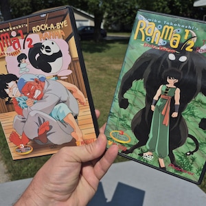 May include: Two Ranma 1/2 DVD cases featuring anime artwork. The left case is titled Rock-A-Bye Ranma and Ranma Forever, showing a red-skinned character holding a person. The right case is titled The Demon from Jusenkyo, featuring a character with a large black creature.
