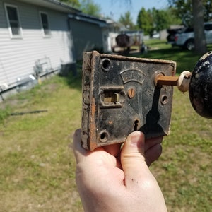 May include: Antique door lock and knob with a black porcelain knob and a metal lock plate with the word "D.L.M." on it.