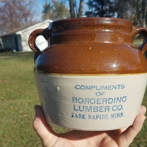 May include: A brown and white ceramic crock with blue lettering that reads "Compliments of Borgording Lumber Co. Park Rapids, Minn."