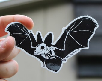 May include: A black and white sticker of a bat skeleton with its wings spread out. The sticker has the text "©2016 FAYETTE STUDIO" in the bottom right corner.