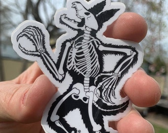 May include: Black and white sticker of a werewolf skeleton with a snarling expression. The sticker is on a white background and has a black outline. The text "sette Studio" is visible at the bottom of the sticker.