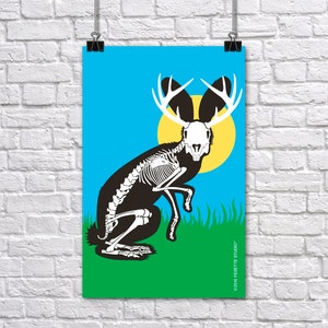 May include: A poster featuring a black and white illustration of a jackalope skeleton with antlers, set against a blue sky and yellow sun. The jackalope is on green grass. The poster is hanging on a white brick wall.
