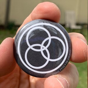 May include: A black button with a white circle design featuring three overlapping circles. The button has the text "© 2019 FESETTE STUDIO" printed on the bottom.