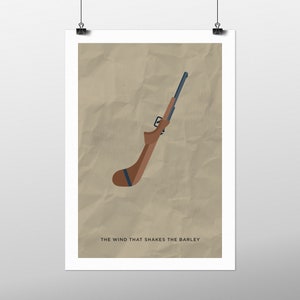 Può includere: Un poster minimalista con un'illustrazione marrone e blu di un fucile. Il testo "THE WIND THAT SHAKES THE BARLEY" è in fondo al poster.