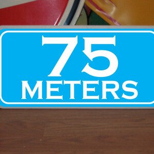 May include: A blue sign with white lettering that reads "75 meters".
