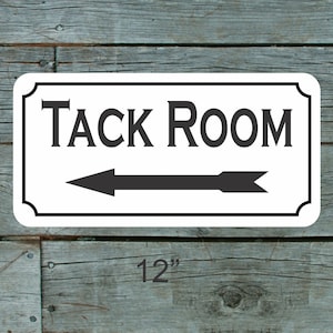 以下が含まれることがあります： 黒枠の白い長方形の看板に「TACK ROOM」という文字と左を向いている黒い矢印が書かれている。看板の幅は30.5cm、高さは15.2cmです。