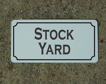 May include: White rectangular sign with a black border and rounded corners. The sign says "STOCK YARD" in black lettering.
