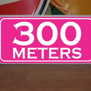 May include: A pink sign with white lettering that reads "300 meters".