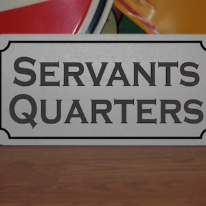 Pode incluir: Uma placa de metal prateada com letras pretas que diz "Servants Quarters".