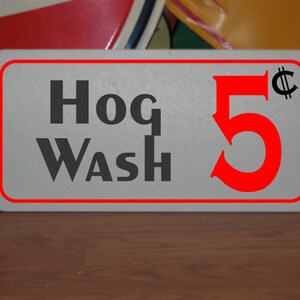 Puede incluir: Un letrero rectangular blanco con borde rojo y texto negro que dice "Hog Wash 5¢".