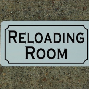 May include: White rectangular sign with black lettering that reads "Reloading Room".