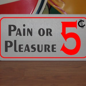 Peut inclure: Une pancarte rectangulaire blanche avec une bordure rouge et du texte noir qui dit "Pain or Pleasure 5&cent;". Le chiffre 5 est rouge et le symbole du cent est noir.