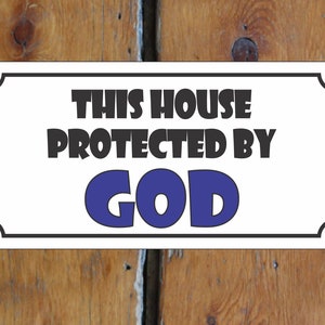 Puede incluir: Un letrero rectangular blanco con borde negro y esquinas redondeadas. El letrero dice "THIS HOUSE PROTECTED BY GOD" en texto negro en negrita, con "GOD" en azul. El letrero está montado en una puerta de madera.