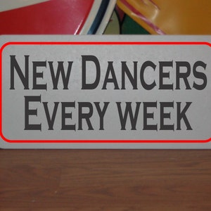 May include: White sign with a red border, featuring the text "NEW DANCERS EVERY WEEK" in black serif font.