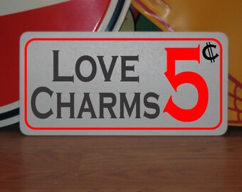 May include: A white sign with a red border and the text "LOVE CHARMS 5¢" in black and red lettering.