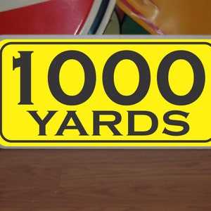 May include: A yellow sign with black text that reads "1000 YARDS".