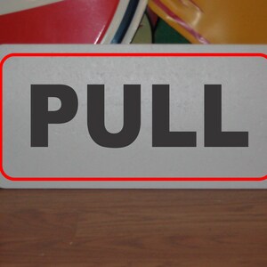 Puede incluir: Un letrero blanco con borde rojo que dice "PULL" en letras negras.