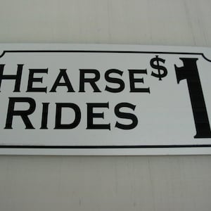 Puede incluir: Señal rectangular blanca con texto negro y borde. La señal dice "Hearse $1 Rides".
