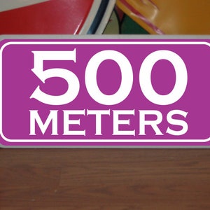 May include: A rectangular sign with a magenta background and white border. The sign displays the number "500" above the word "METERS" in white, sans-serif font. The sign is likely used for distance indication, with 500 meters being approximately 1640 feet.