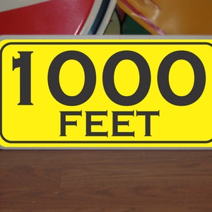 May include: A yellow sign with black text that reads "1000 FEET".