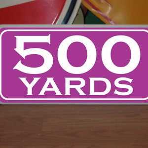 May include: Purple sign with white text that reads "500 YARDS".