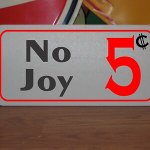 May include: A white sign with a red border and red text that says "No Joy 5¢".