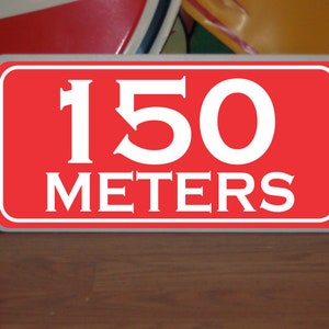 May include: Red rectangular sign with white border and white text that reads "150 METERS".