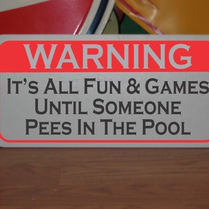 May include: A white sign with a red border and the text "WARNING IT'S ALL FUN & GAMES UNTIL SOMEONE PEES IN THE POOL" in black.
