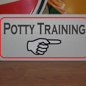 May include: White sign with a red border and the text "POTTY TRAINING" in black. A black and white pointing hand is below the text.