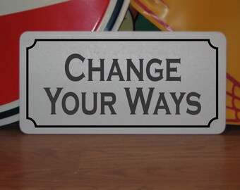 May include: A white metal sign with black lettering that reads "CHANGE YOUR WAYS".