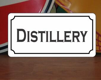 Könnte beinhalten: Weißes Schild mit schwarzem Rand und abgerundeten Ecken. Auf dem Schild steht das Wort "DISTILLERY" in schwarzer Serifenschrift.