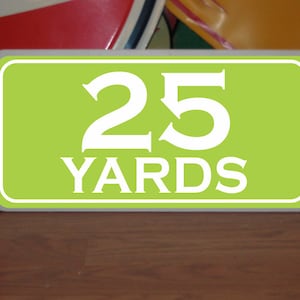 May include: A green rectangular sign with white text that reads "25 YARDS".
