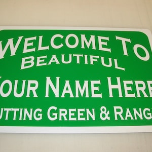 Puede incluir: Señal verde y blanca con el texto "Bienvenido a Beautiful [Tu Nombre Aquí] Putting Green & Range".