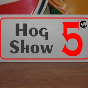 Puede incluir: Un letrero blanco con borde rojo y texto negro que dice "Hog Show 5¢".