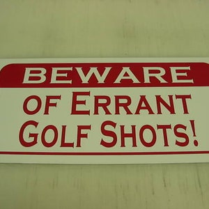 May include: White sign with red border and the text "BEWARE OF ERRANT GOLF SHOTS!"