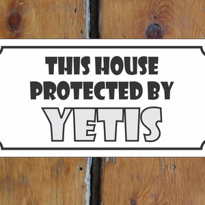 Puede incluir: Un cartel blanco con borde negro y esquinas redondeadas. El cartel dice "This house protected by Yetis" en letras negras y grises.