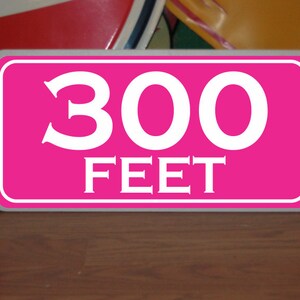 May include: A pink sign with white lettering that reads "300 FEET".