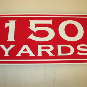 May include: Red rectangular sign with white text that reads "150 YARDS".