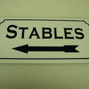 以下が含まれることがあります： 左向きに黒い矢印と黒い文字で書かれた白い看板。看板には「STABLES」と書かれている。