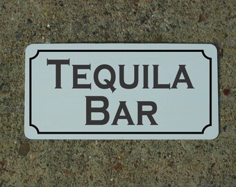 May include: White rectangular sign with black border and black text that reads "Tequila Bar".