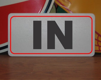 May include: A white sign with a red border and the word "IN" in black letters.