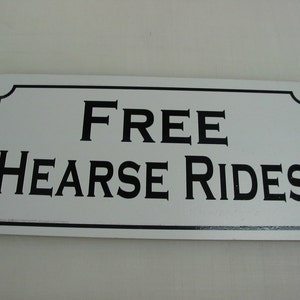 Może przedstawiać: Biały prostokątny znak z czarną ramką i czarnym tekstem, który brzmi "FREE HEARSE RIDES".