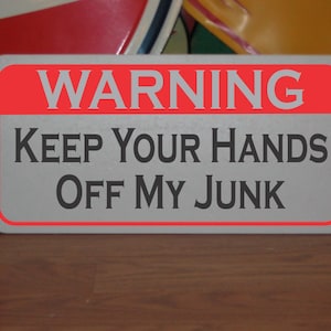 May include: A white metal sign with a red border and the text "WARNING KEEP YOUR HANDS OFF MY JUNK" in black.