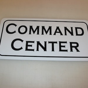 May include: White rectangular sign with black text that reads "COMMAND CENTER".